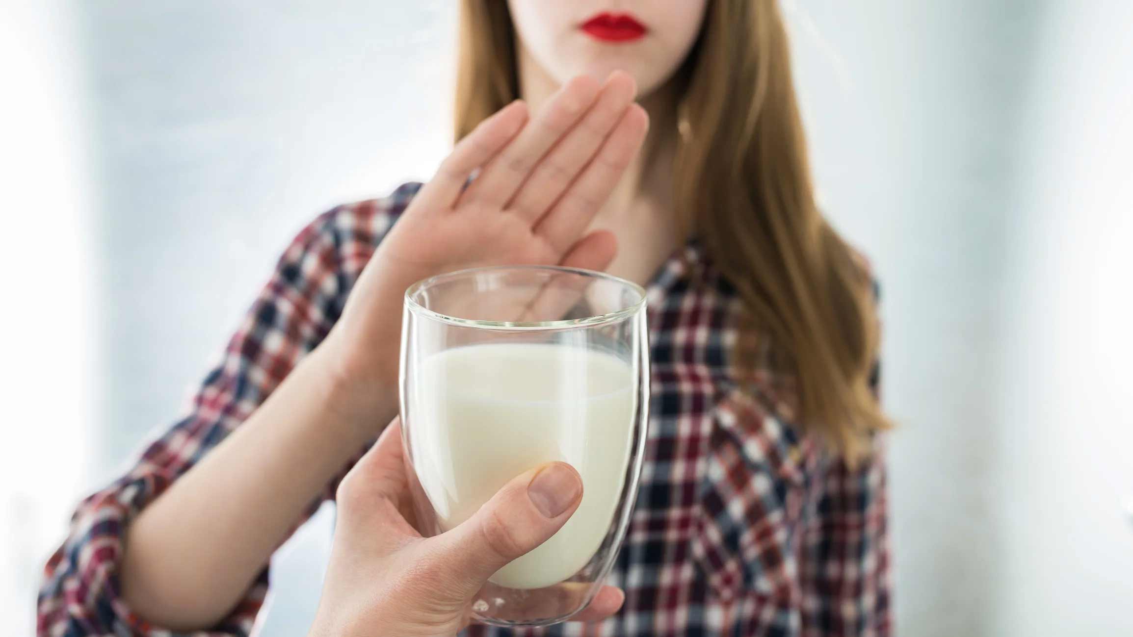 woman holding her hand up to a glass of milk being offered to her