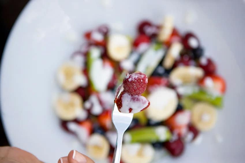 A raspberry on a fork held over a bowl of fruit