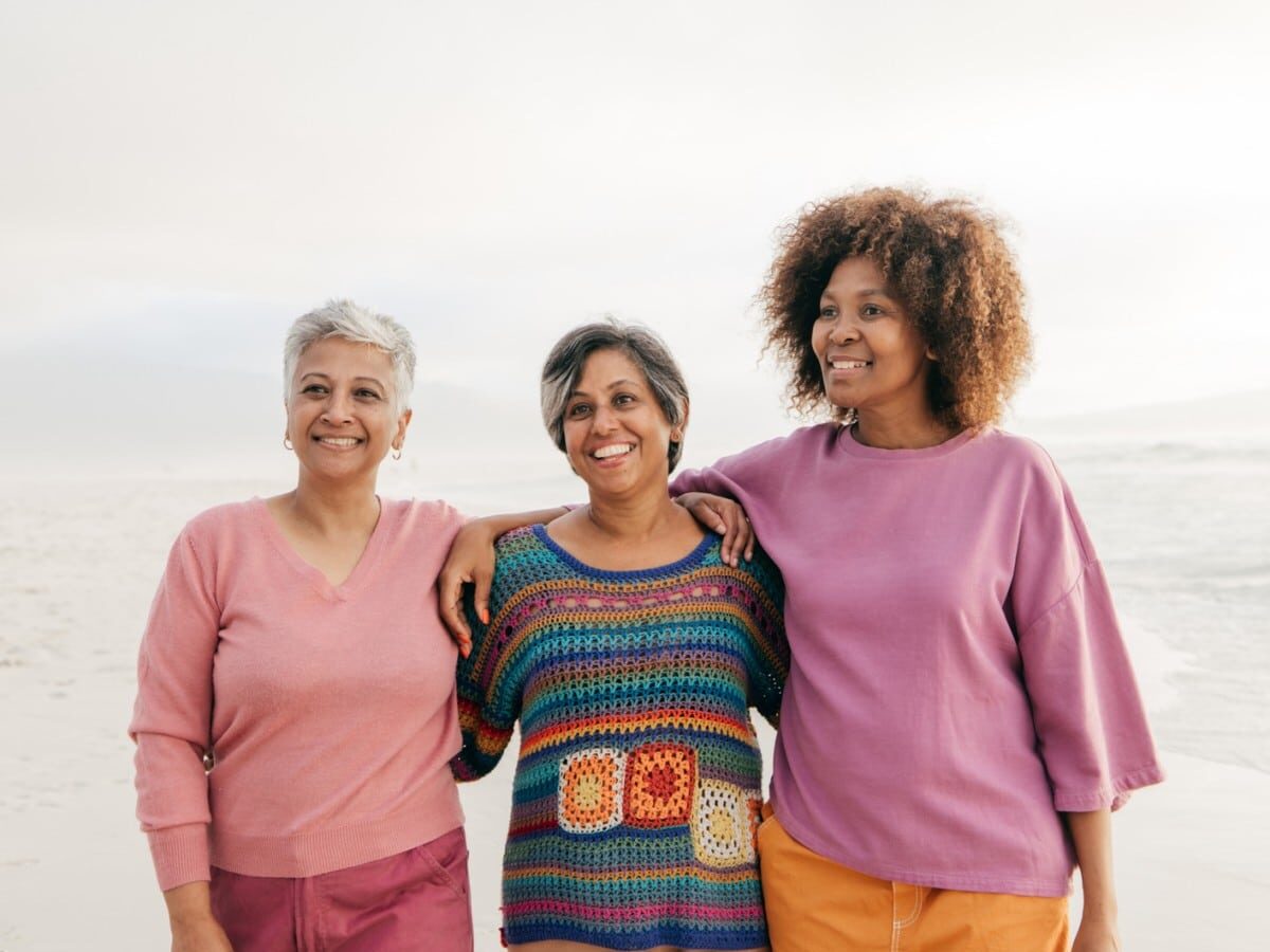 Three women smiling on a beach.