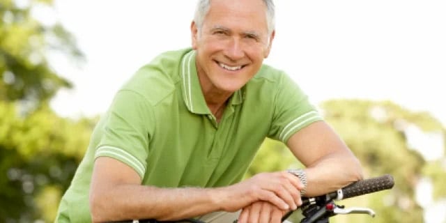 Elderly man smiling while leaning on a bike