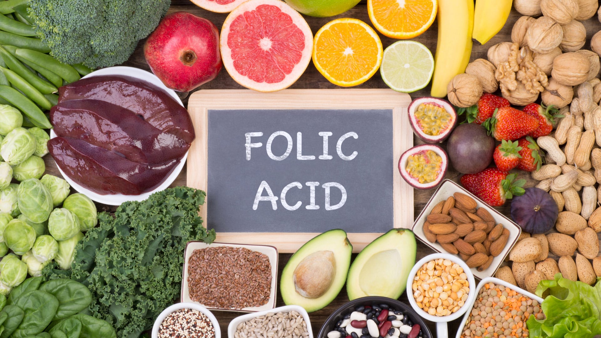 folic acid written on a chalkboard surrounded by nuts and fruit